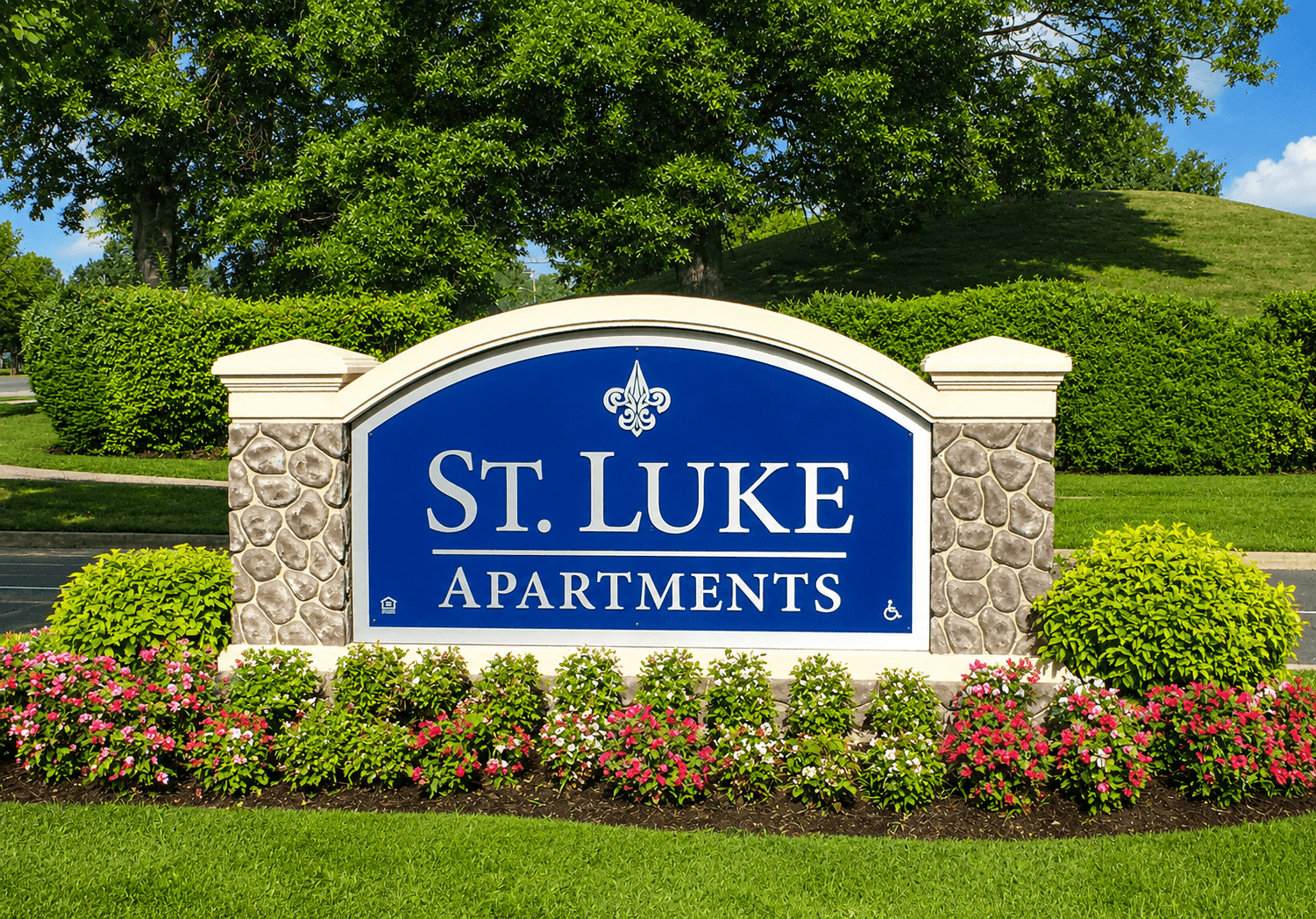 A sign for St. Luke Apartments is surrounded by flowers and greenery.